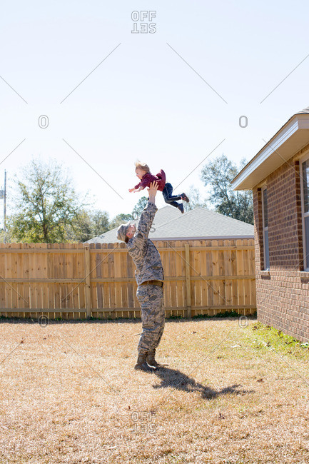 Male soldier lifting up daughter in garden at air force military base