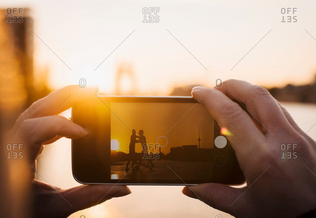 Person taking photograph of Molecule Man sculpture at sunset, Spree River, Berlin, Germany