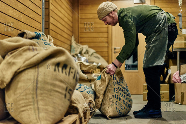 Male coffee shop owner lifting sack of coffee beans in store room