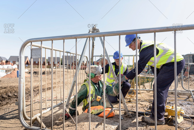 Apprentice builders assisting worker out of manhole on building site