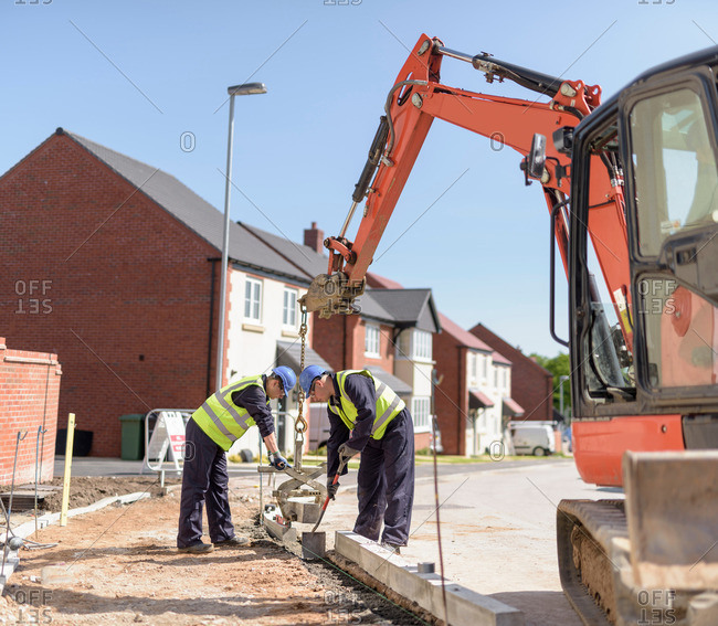 Builders using digger to lift curb stones on housing building site