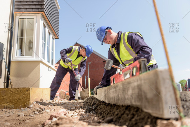 Apprentice builders using digger to lift curb stones on housing building site