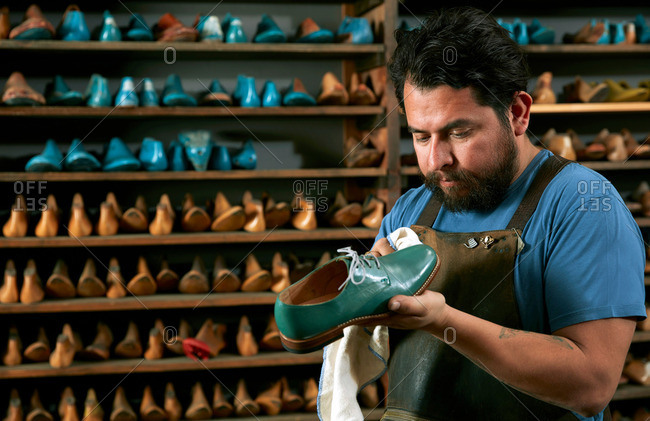 Male cobbler in traditional shoe shop polishing green brogue
