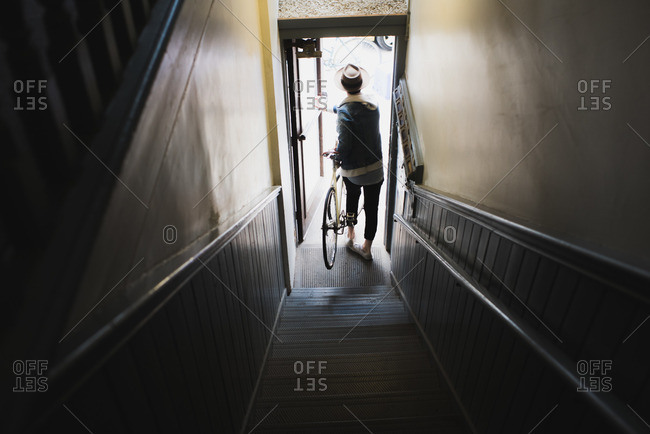 Young man at bottom of stairs, exiting building with bike, elevated view