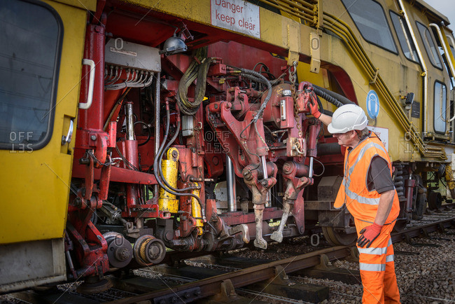 Railway worker inspecting tamping machine on railway