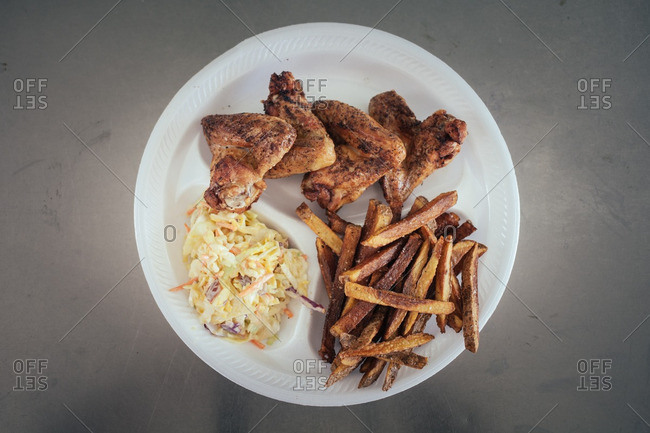 Chicken wings, fries and coleslaw on a disposable plate