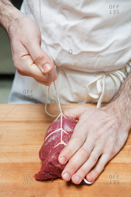 Butcher tying beef tenderloin with string on butcher block
