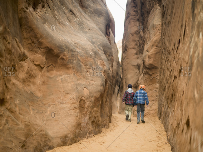 Two boys exploring a narrow canyon off the Devil\'s Playground Trail in Arches National Park, Moab, Utah