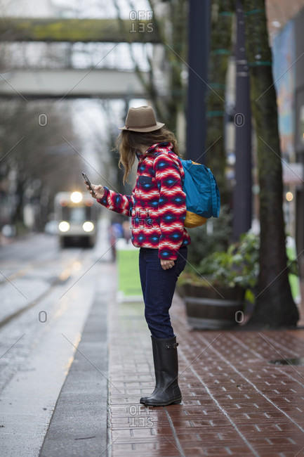 A woman with a cell phone standing by a street, waiting for a train in Portland, Oregon