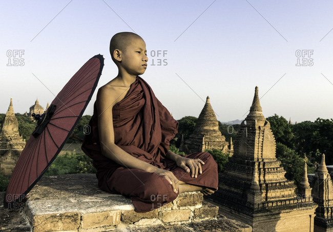 Young novice Buddhist monk sitting on a temple top with a  parasol