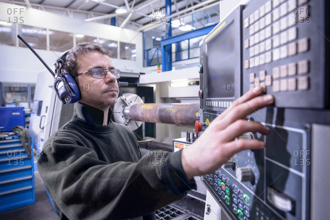 Engineer in ear defenders setting controls on industrial lathe