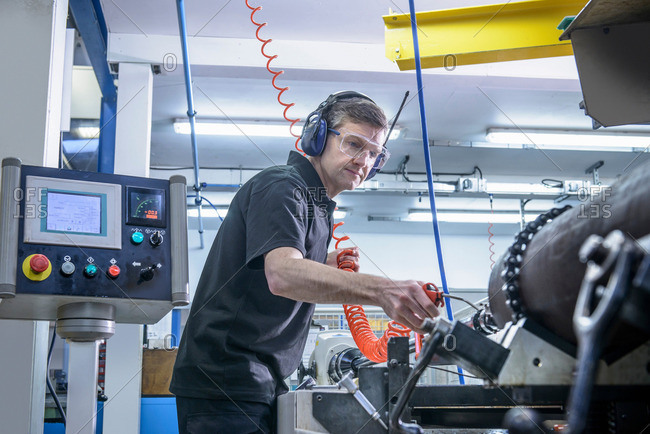 Engineer in ear defenders and safety glasses cleaning steel bar on lathe