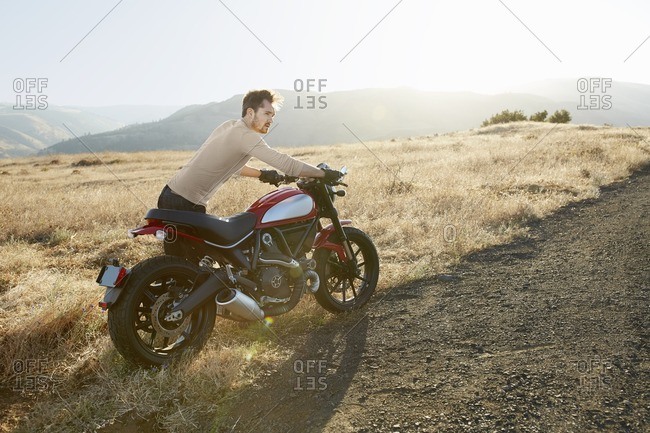 Man pushing motorcycle in rural setting