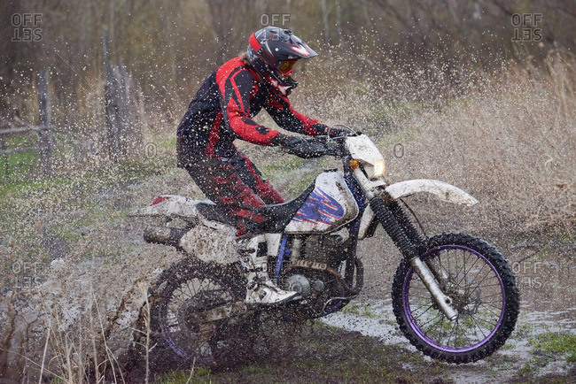 Motocross rider splashing through puddles in the countryside