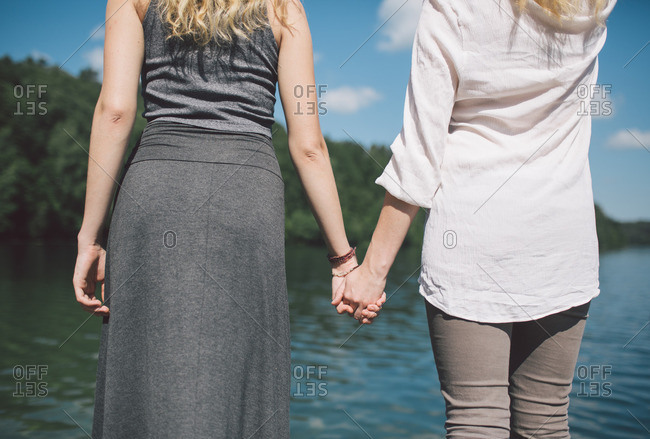 Close up of two women holding hands by a lake