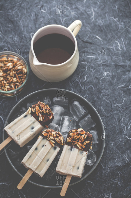 Almond butter blueberry popsicles on an iced tray with a pitcher of melted chocolate