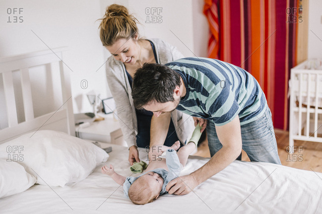 Parents with baby boy- lying on bed- dressing
