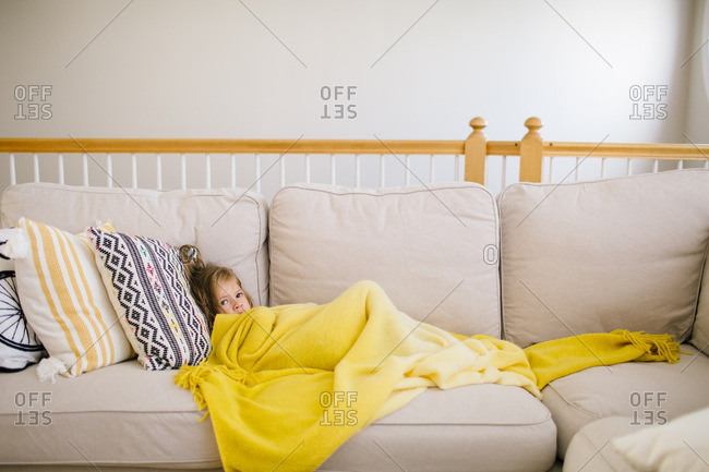 Sick little girl resting on a couch with yellow blanket