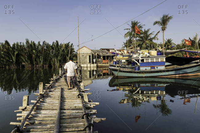 Man walking across bamboo dock next to fishing boats, Vietnam