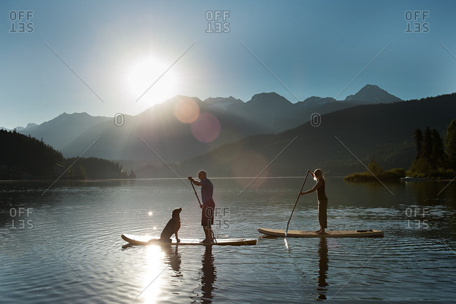 People and dog stand up paddle boarding on a mountain lake at sunrise