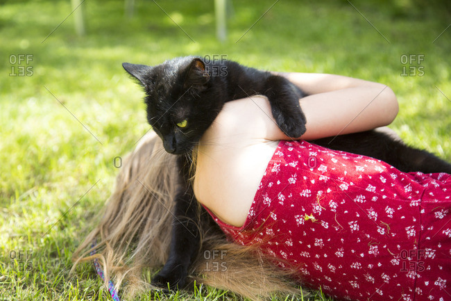 Back view of little girl lying on meadow with black cat