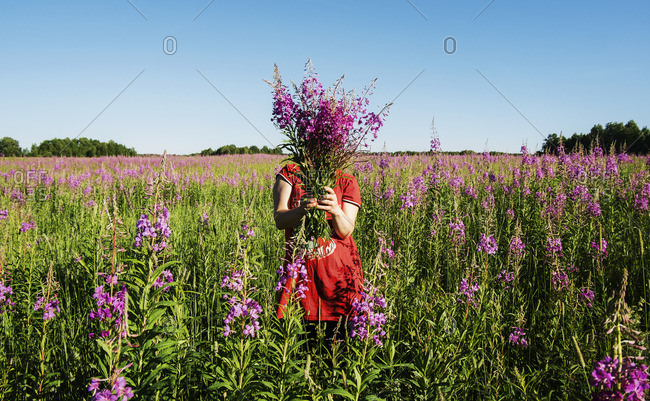 Female farmer hiding face with flowers on farm against clear blue sky