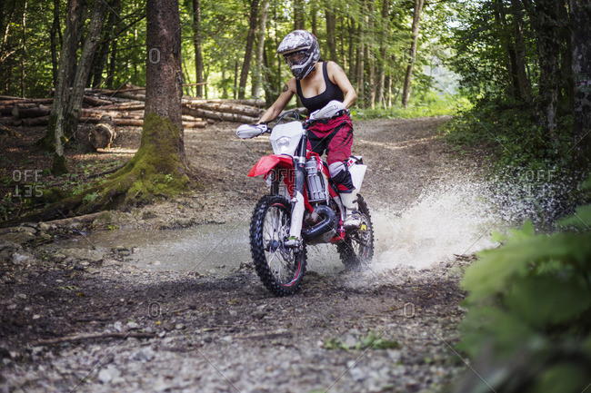 Female biker riding dirt bike on puddle in forest