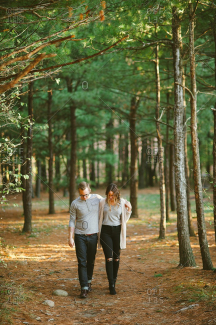 Couple walks with arms around each other in woods