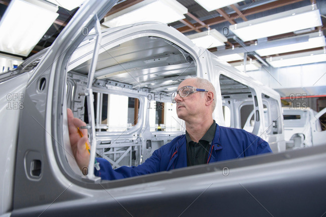 Worker inspecting paint finish of vehicle in car factory