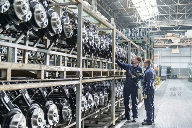 Workers inspecting large number of axles on shelving unit