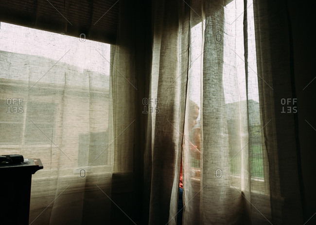 Boy looking out window from behind curtains