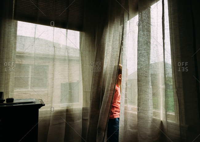 Young boy looking out window from behind curtains