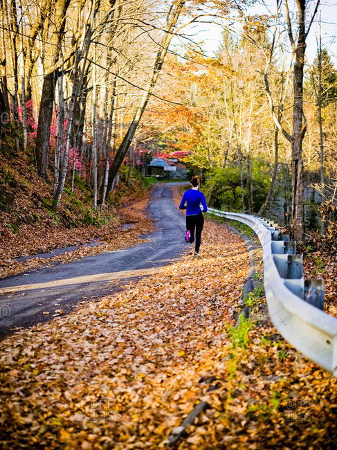 Woman running along a road in fall leaves