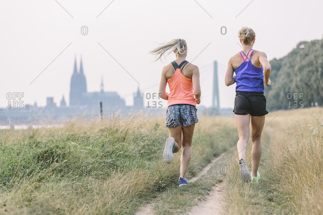 Two young women running on field path