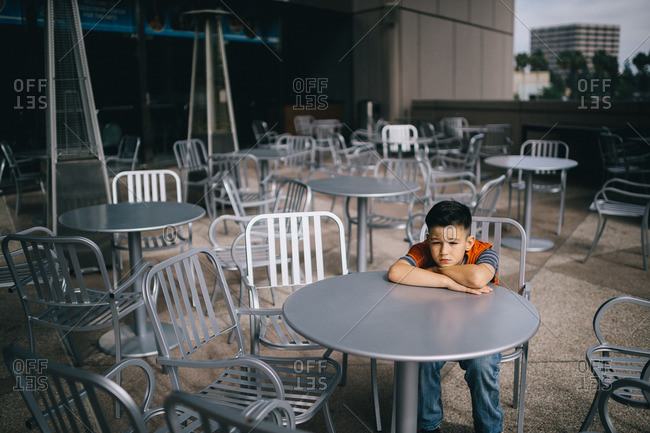 Boy sitting at table in outdoor dining area of building