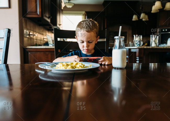 Little boy playing games on a smartphone during breakfast