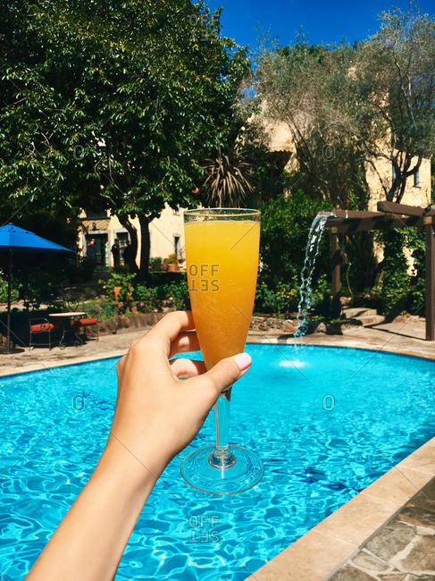 Woman\'s hand with mimosa cocktail toasting at luxury pool area of resort