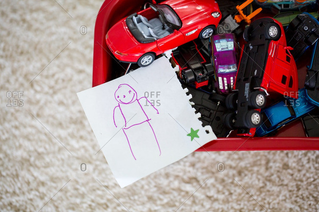 Child\'s drawing on a piece of paper set on top of a bin full of toy cars
