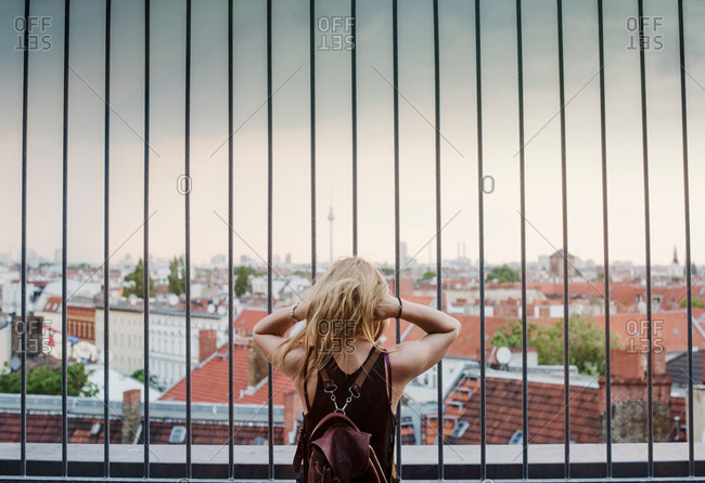 Young woman looking through railings, at view across rooftops, rear view