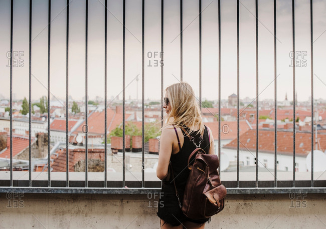 Young woman looking through railings, at view across rooftops, rear view