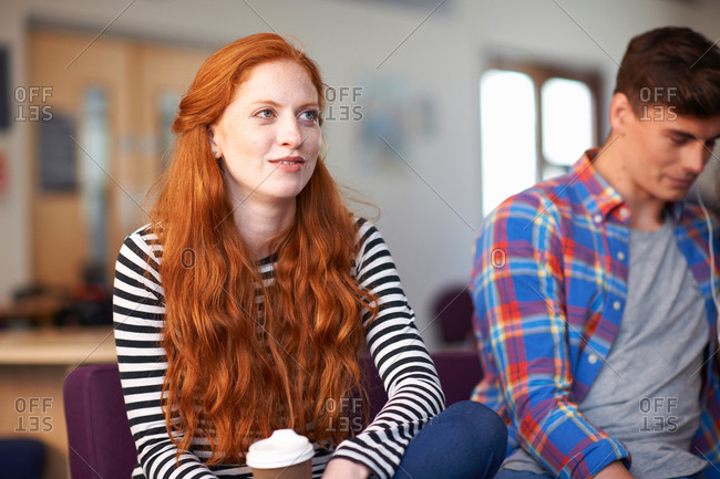 Young female college student sitting with takeaway coffee in common room
