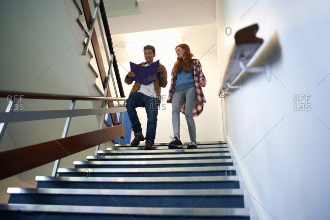 Young male and female college students moving down stairway reading file