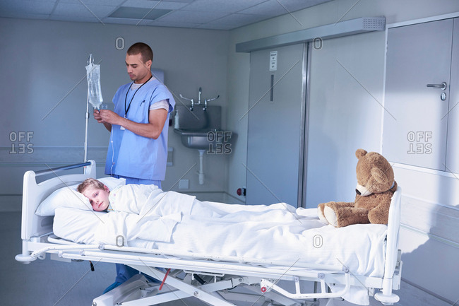 Male nurse adjusting intravenous drip for boy patient in hospital children\'s ward