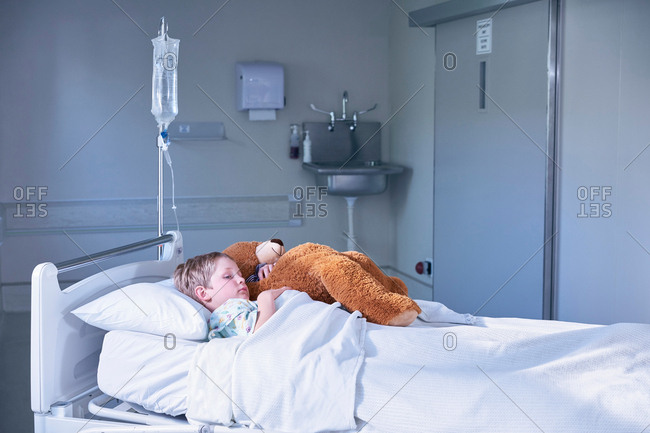 Boy patient in bed hugging teddy bear on hospital children\'s ward