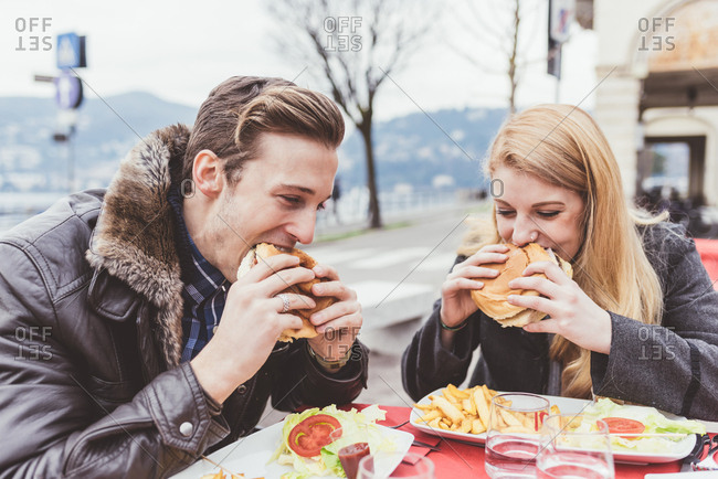 Young couple eating burgers at sidewalk cafe, Lake Como, Italy