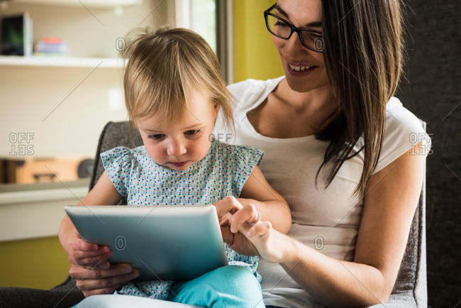 Mother teaching daughter to use digital tablet at home