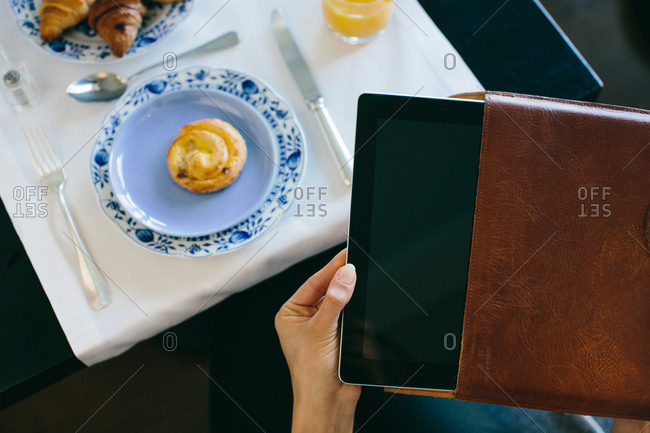 Woman's hand removing digital tablet from case whilst having  breakfast at  boutique hotel in Italy
