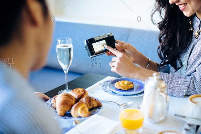 Young woman pointing at digital camera whilst having champagne breakfast at  boutique hotel in Italy