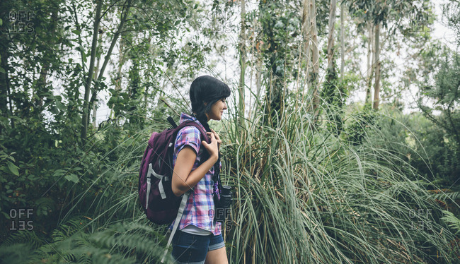 Smiling young woman with backpack walking in the forest