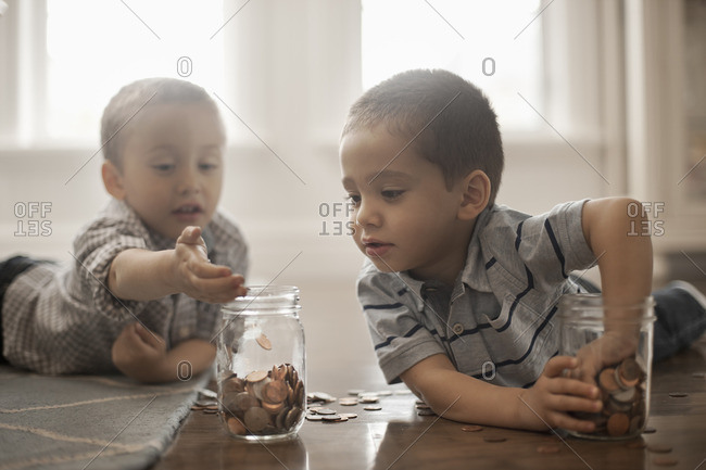 Two children playing with coins, dropping them into glass jars